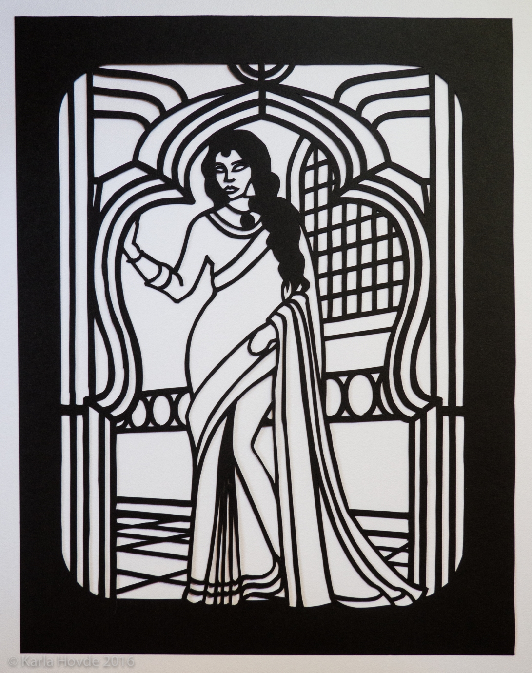 Paper cutting art in black paper shows stylized woman wearing a sari standing in South Asian style doorway arch.